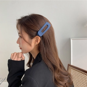 Matte blue rectangular hair clip worn by a model in a minimalist lifestyle setting