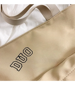 Close-up of beige canvas tote bag with black DUO NING letter embroidery and woven texture