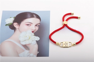 Detail of red braided rope bracelet with gold star-patterned lock charm and pavé crystals