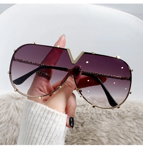 Macro detail of oversized V-logo sunglasses with purple gradient lenses and gold frame