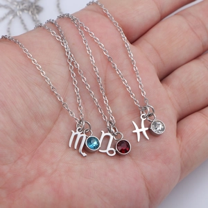 Three silver stainless steel zodiac necklaces with colorful birthstones held in hand