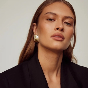 Gros plan sur des boucles d'oreilles dorées ovales portées par un mannequin chic