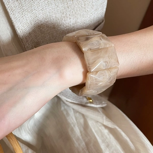 Detail of a chunky acrylic marble bangle featuring beige and cream swirling textures