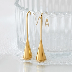 Elegant gold drop earrings in long teardrop shape on a minimalist water bubble background