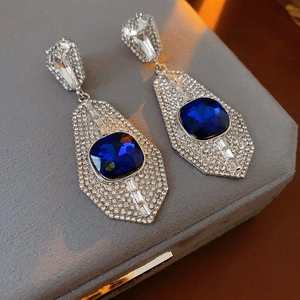 Close-up of geometric silver earrings with blue gemstones and sparkling rhinestones