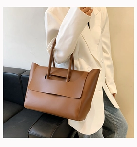 Detail view of a large brown vintage leather tote bag carried by a model in a minimal setting
