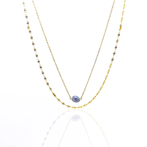 Detail of double-layer gold necklace featuring a blue stone pendant and olive leaf chain
