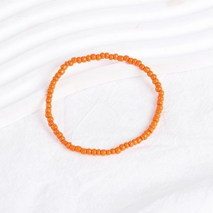 Detailed close-up of a vibrant orange seed bead bracelet on a white textured background