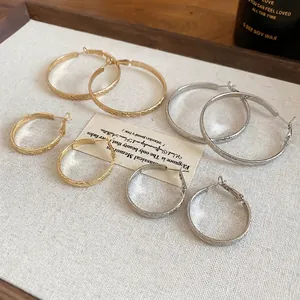 Polished silver and gold hoop earrings set with textured diagonal stripes on white backdrop