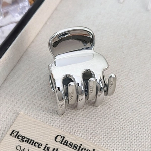 Detail of silver metallic heart hair claw clip with mirror finish on beige fabric