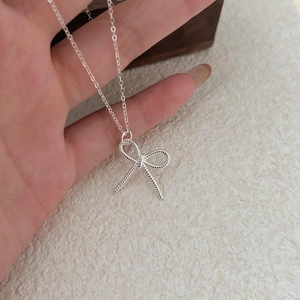 Close-up of a silver bow necklace with woven rope texture held against a textured wall
