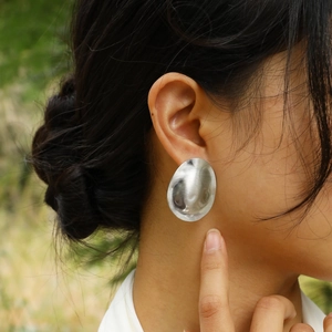 Close-up of a model wearing large silver textured oval earrings in a natural setting