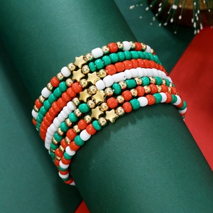 Détail de bracelets de Noël en perles colorées sur socle vert avec breloques étoiles