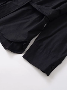 Detail view of the curved hem and button cuffs on this black long sleeve utility shirt
