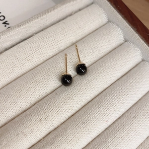 Macro detail of geometric black round bead earrings with gold plating on a beige velvet tray