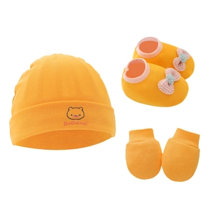 Orange cotton knit baby set with bear hat, bow booties, and mittens on white background