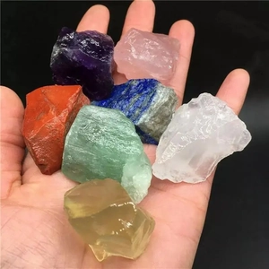 Set of 7 natural raw crystal stones in various colors held in hand over black background
