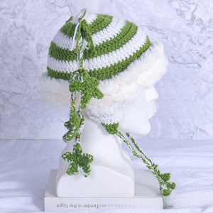 Detailed close-up of green and white striped crochet hat with plush trim and star charms