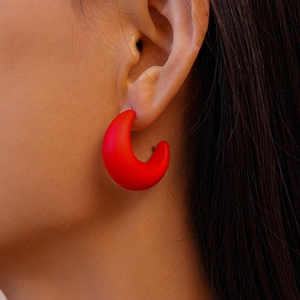 Close-up of matte red C-shaped acrylic earrings worn by a model in natural light
