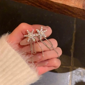 Detail of silver snowflake earrings with pearl center and elegant tassel chain held by hand