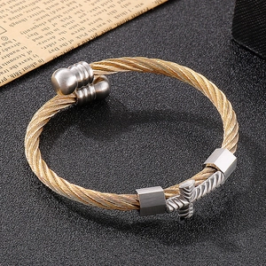 Detail of gold twisted wire cable bracelet featuring a silver cross charm and end beads
