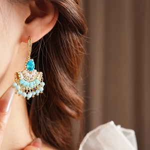 Vue détaillée de boucles d'oreilles éventail bleues avec perles et pompons sur modèle