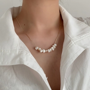 Close-up of minimalist gold necklace with curved freshwater pearl pendant on a model
