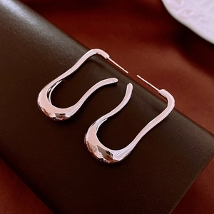 Macro detail of irregular silver hoop earrings with wavy texture and high-polish finish