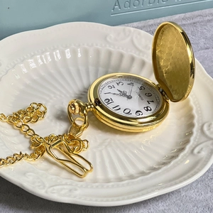 Detail of vintage gold pocket watch with quartz movement and decorative chain on ceramic