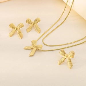 Detail of 18K gold-plated bow necklace and stud earrings set on textured fabric