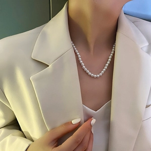 Dettaglio di un'elegante collana di perle con fiocco indossata da modella con blazer