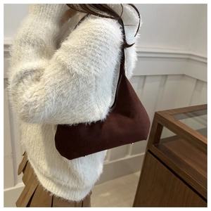 Detail of a dark brown suede underarm bag with zipper closure on a white sweater