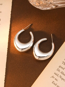 Close-up of silver C-shaped chunky metal earrings with mirror finish on vintage desk