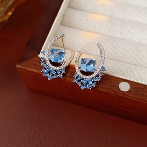 Close-up of silver U-shaped earrings with square blue crystal in a jewelry box