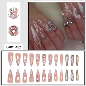 Long almond press-on nails with white floral patterns and 3D rhinestones