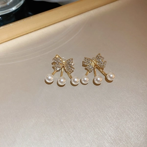 Dettaglio di orecchini a fiocco dorato con strass lucidi e perle a forma di ciliegia
