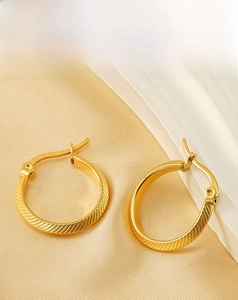 Close-up of gold plated stainless steel hoop earrings with textured striped pattern