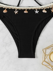 Detail of black bikini bottoms with seashell pendants and woven lace on marble background