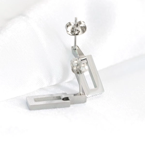 Macro shot of silver brushed stainless steel hollow rectangular stud earrings on silk