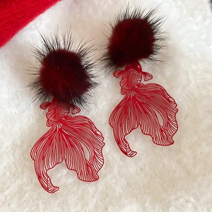 Macro detail of red hollowed-out koi fish earring with plush pom pom on soft white texture