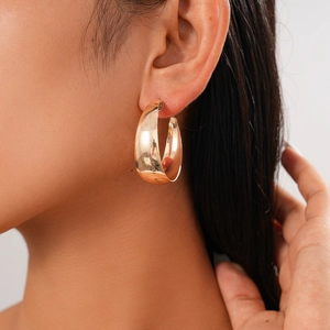 Close-up of minimalist golden circular earring on model showing high gloss metallic finish
