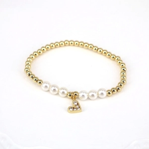Detailed macro view of gold round beads and white pearl bracelet with heart pendant charm