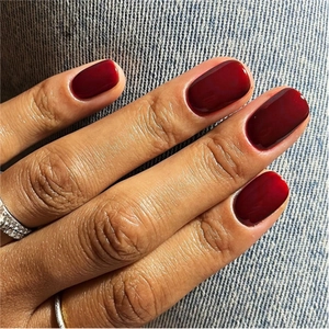 Close-up of glossy deep red medium long square artificial nails on denim background
