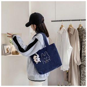 Detail of dark blue corduroy tote bag with rabbit embroidery and plush charm on model