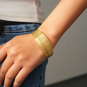 Detail of layered gold bangles featuring a shimmering textured surface on a model's wrist