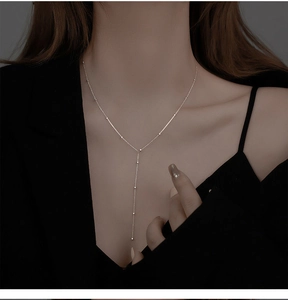 Close-up of silver Y-shaped tassel necklace with small beads worn on a model