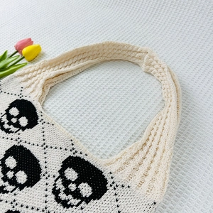 Close-up of cream knit tote bag featuring a black skull jacquard and braided shoulder strap