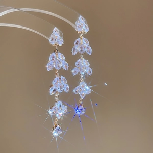 Detailed macro view of gold tassel earrings with sparkling teardrop crystals on beige backdrop