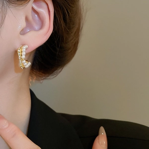 Detail view of double-layer C-shaped pearl and rhinestone earrings on a model