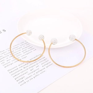 Detail of two gold C-shaped open bracelets with sparkling rhinestone-encrusted balls